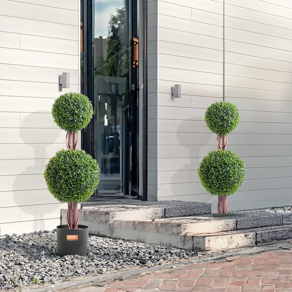 Three potted topiary plants in front of a modern building entrance.