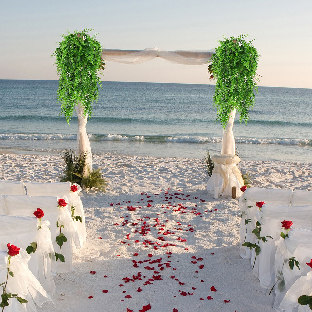 Beach wedding setup with floral arches and rose petals leading to the ocean.