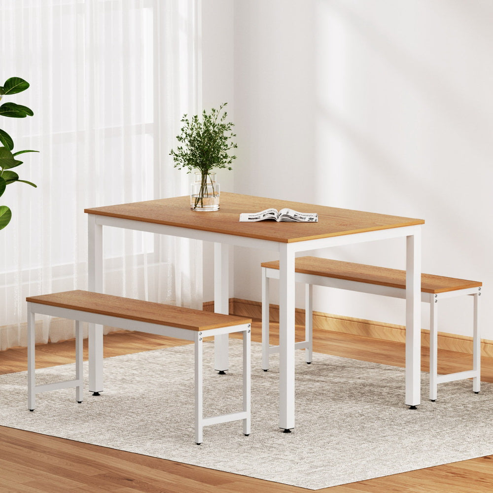 Dining table set with benches in a room with white walls and wooden flooring.